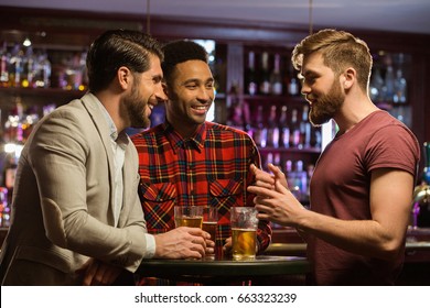 Young Happy Men Drinking Beer And Talking In Cafe Or Pub