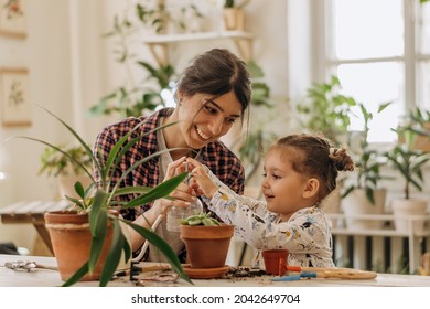 Young Happy Mixed Race Woman With A Three-year-old Daughter Is Transplanting Houseplants At Home.Home Gardening.Family Leisure, Hobby Concept.Biophilia Design And Urban Jungle Concept.