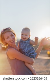 Young happy mother dandling her cute baby girl while hanging out outdoors. Young woman holding a baby girl on hands on the beach - Shutterstock ID 1823186405