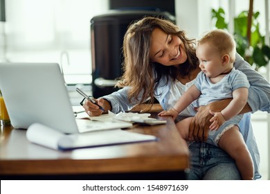 Young Happy Mother Going Through Home Finances And Communicating With Her Baby Son. 