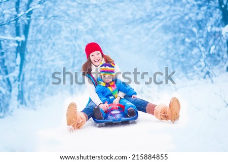Young happy mother and her little toddler daughter enjoying a sledge ride in a beautiful snowy winter park 