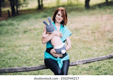 Young happy mother holding newborn baby boy in her hands outdoors in summer in sun rays, baby boy in rabbit costume - Powered by Shutterstock