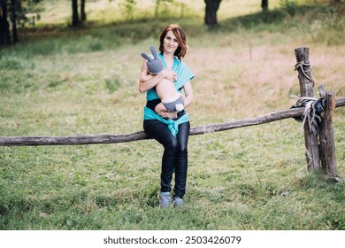 Young happy mother holding newborn baby boy in her hands outdoors in summer in sun rays, baby boy in rabbit costume - Powered by Shutterstock