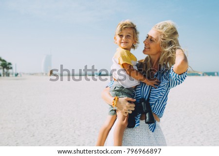 Young happy mother with little blonde son on the beach