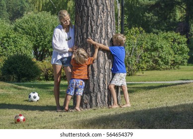 Young happy mother playing with two kids near the tree