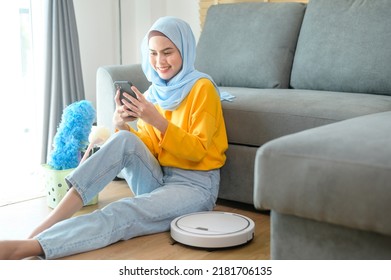 A Young happy muslim woman relaxing and using smartphone in living room while Robotic vacuum cleaner working - Powered by Shutterstock