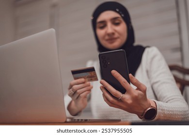 A young happy Muslim woman using mobile phone and holding credit card checking balance account or making money transfer. Online Payment Internet Banking Concept.  - Powered by Shutterstock