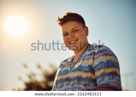 Young happy non-binary woman against the sky looking at camera. 