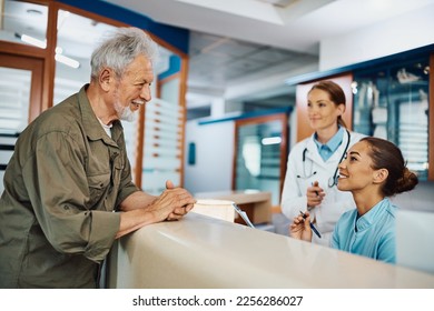 Young happy nurse taking notes while communicating with mature patient at reception desk at medical clinic. - Powered by Shutterstock