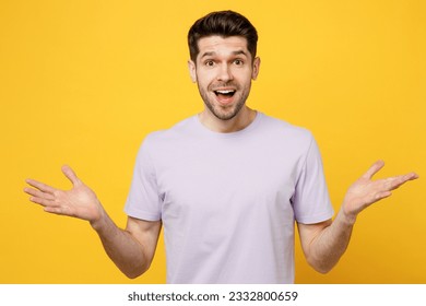 Young happy overjoyed exultant jubilant caucasian man wear light purple t-shirt casual clothes look camera spread hands say wow isolated on plain yellow background studio portrait. Lifestyle concept