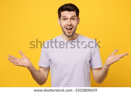 Young happy overjoyed exultant jubilant caucasian man wear light purple t-shirt casual clothes look camera spread hands say wow isolated on plain yellow background studio portrait. Lifestyle concept
