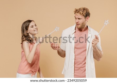 Young happy parent man with child teen girl wear casual clothes Daddy kid daughter hold princess magic wand feia stick playing isolated on beige background studio. Father's Day birthday family concept