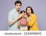 Young happy parents mom dad with child kid girl 6 years old wear blue yellow casual clothes watch movie film eat popcorn, cover daughter eyes isolated on plain purple background. Family day concept