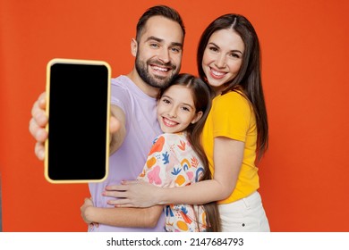 Young happy parents mom dad with child kid daughter teen girl in basic t-shirts hold use mobile cell phone with blank screen workspace area isolated on yellow background studio. Family day concept. - Shutterstock ID 2147684793