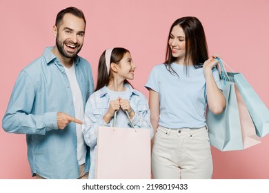 Young Happy Parents Mom Dad With Child Kid Daughter Teen Girl In Blue Clothes Holding Point Index Finger On Package Bags With Purchases After Shopping Isolated On Plain Pastel Light Pink Background.