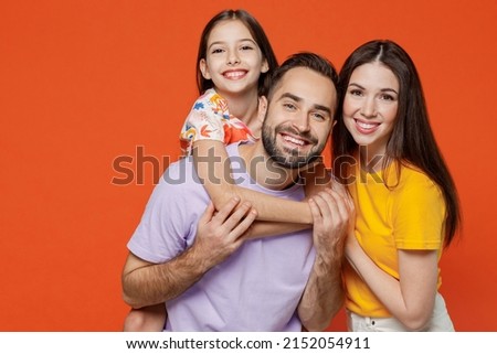 Young happy parents mom dad with child kid daughter teen girl wear basic t-shirts giving piggyback to daughter isolated on yellow background studio portrait. Family day parenthood childhood concept.