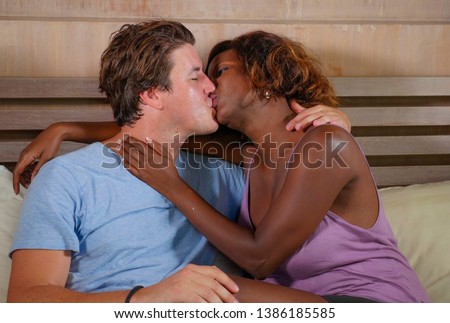 young happy and passionate mixed ethnicity couple in love kissing and smiling on bed with attractive black afro American girlfriend or wife and handsome white man in multi racial relationship
