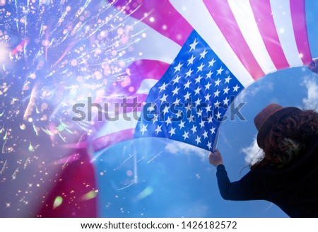 Young happy patriot girl holding the american flag under the 4th of July fireworks. 