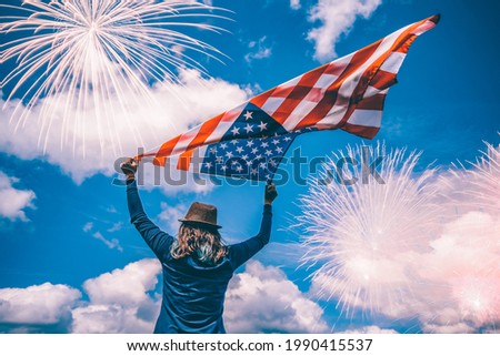 Young happy patriot girl holding the american flag under the 4th of July under fireworks. 