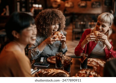 Young happy people having lunch together. Focus on a women biting a burgers - Powered by Shutterstock