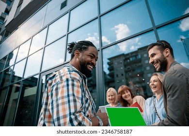 Young happy people on start-up meeting against modern glass office building. Diverse Millennials using laptop with green chroma key on screen. Copy space - Powered by Shutterstock