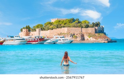 Young happy and playful red hair woman in blue bikini swimming on the turquoise sea playing with waves enjoying summer holidays Pigeon Island with a "Pirate castle" Kusadasi harbor - Aegean coast  - Powered by Shutterstock