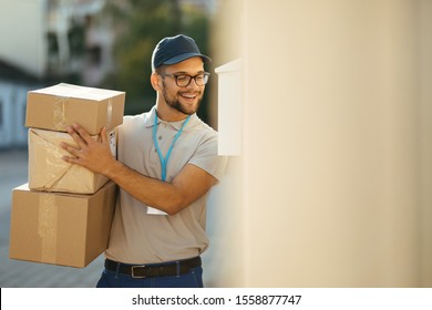 Young Happy Postal Worker Delivering Packages And Talking With Customer Over The Intercom.  Copy Space. 