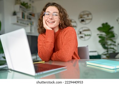Young happy pretty business woman student sitting at desk at home office with laptop computer looking at camera advertising online learning, remote work, business webinars. Portrait.