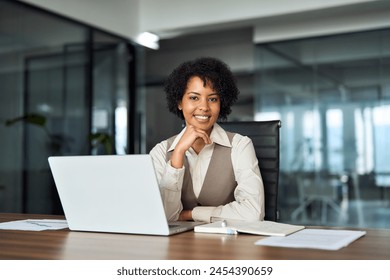 Young happy professional African American business woman working on laptop in office sitting at desk looking at camera, female company manager executive portrait at workplace. - Powered by Shutterstock