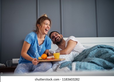 Young Happy Relaxed Couple Having Breakfast Together In Bed. Having Fun And Smiling.