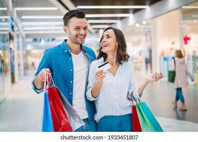 Young Happy Roamntic Couple With Shopping Bags And Credit Card In The Mall, Having Fun Making Purchases Together Enjoying Black Friday Sale.