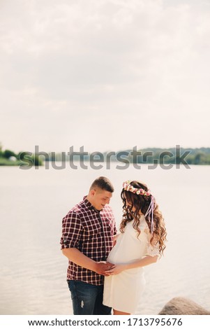 Young happy romantic pregnant couple hugging on nature near lake in summer park. Pregnant woman expecting a baby. Future mom and dad, family. mother's, father's day