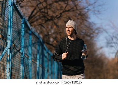 Young Happy Runner Carrying Bottle Of Water While Jogging Outdoors. 