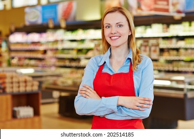 Young Happy Saleswoman With Red Apron In A Supermarket