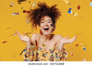 Young happy satisfied excited fun surprised amazed woman 20s with culry hair in casual clothes tossing throwing confetti isolated on plain yellow background studio portrait. People lifestyle concept