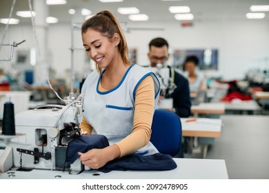 Young happy seamstress working in textile factory and sewing fabric.