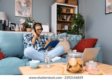 Young happy self loved independent woman lady reading a book at home, sitting on sofa, enjoying free time. Strong satisfied female reader read a story, spending quality time on her day off from work.
