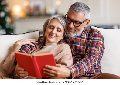 Young happy senior family couple in love enjoying winter holidays together at home, smiling elderly man and woman read book and embrace while relaxing on cozy sofa, spending leisure time on Christmas - Powered by Shutterstock