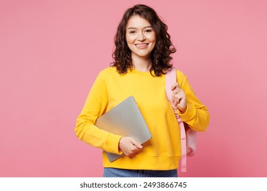 Young happy smart teen girl IT student she wear yellow casual clothes backpack bag hold closed laptop pc computer isolated on plain pastel light pink background. High school university college concept