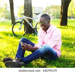 Young happy smiling african american with mobile phone and bicycle behind him in a park - Powered by Shutterstock