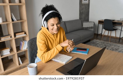 Young Happy Smiling African American Adult Student Wearing Headphones Having Virtual Education Class Meeting Online Call E Learning Webinar On Laptop At Home Office Writing Notes.