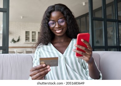 Young Happy Smiling African Black Woman Holding Credit Card And Using Cell Mobile Phone. Businesswoman Working At Home. Online Shopping, Ecommerce, Internet Banking, Spending Money Concept.