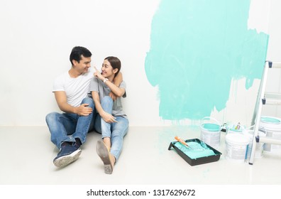 Young Happy Smiling Asian Couple Renovating Their New Home After Painting A Room In Their New House On The Floor. Repair, Building And Home Concept