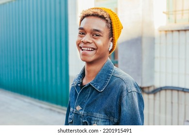 Young happy smiling boy with curly hair listens music on headphones at street dressed in denim jacket and yellow beanie hat. Technology concept. - Powered by Shutterstock