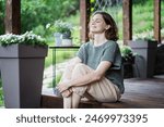 Young happy smiling Caucasian woman sitting on the wooden terrace of a country house enjoying the summer weather