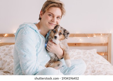 Young Happy Smiling Caucasian Woman With Cute Puppy Dog Pet At Home. Pet Owner Celebrating Christmas Holiday Alone. Holiday Celebration Together With Furry Little Friend. Funny Holiday Gift.