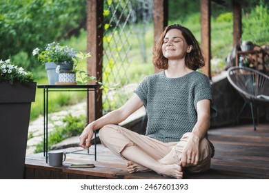 Young happy smiling Caucasian woman sitting on wooden terrace in lotus position, enjoying summer - Powered by Shutterstock