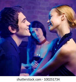 Young happy smiling couple and woman looking at them at club. Focus on couple.