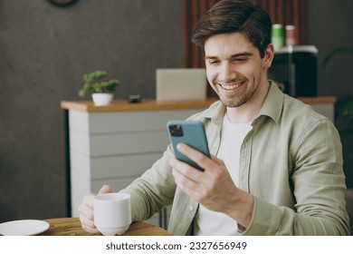 Young happy smiling european man wearing casual clothes sits alone at table in coffee shop cafe restaurant indoors work hold use mobile cell phone chatting drink tea rest relax during free time inside - Powered by Shutterstock