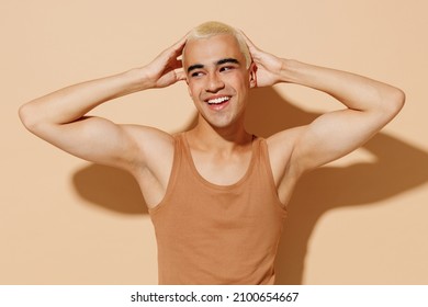 Young Happy Smiling Fun Blond Latin Hispanic Gay Man 20s With Make Up In Beige Tank Shirt Posing With Raised Up Hands Look Aside Isolated On Plain Light Ocher Background Studio People Lgbt Concept.